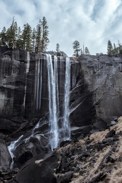 Hermoso paisaje de una poderosa cascada que fluye a través de un acantilado rocoso bajo un cielo nublado