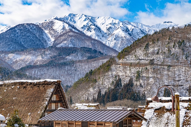 Hermoso paisaje de techos de aldea, pinos y montañas cubiertas de nieve en Japón