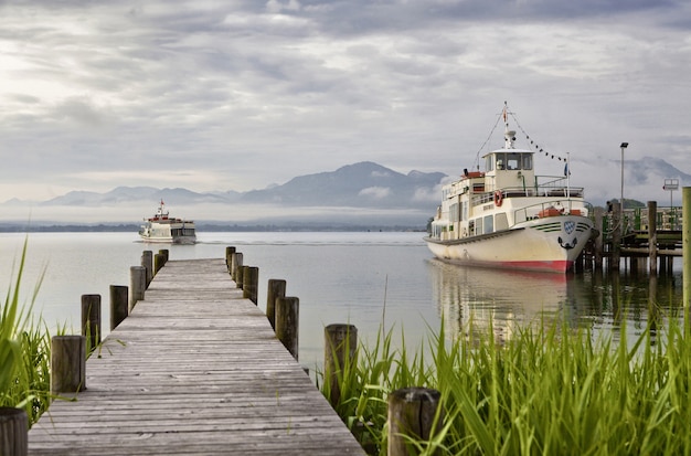 Hermoso de una plataforma de madera que conduce al mar con montañas y barcos al fondo