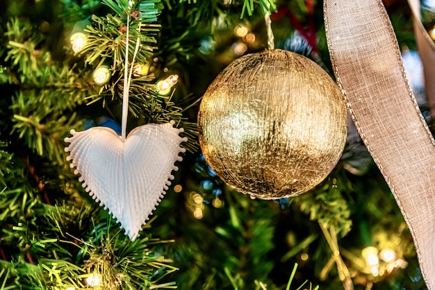 Hermoso primer plano de un adorno en forma de corazón blanco y bola de oro en un árbol de Navidad