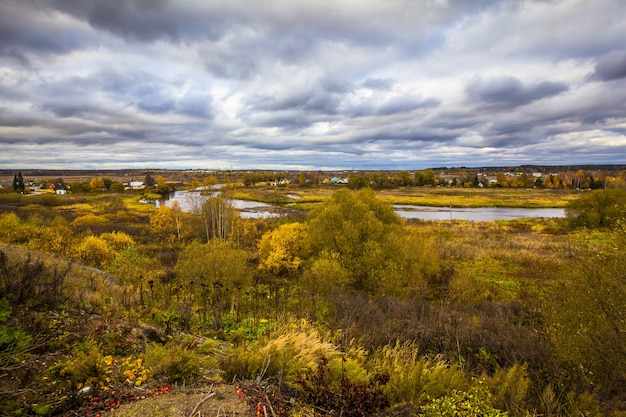 Hermoso pueblo en Rusia en otoño, con los hermosos árboles amarillos bajo el cielo nublado