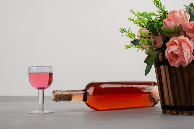 Hermoso ramo de flores y una botella de vino rosado en la mesa gris.