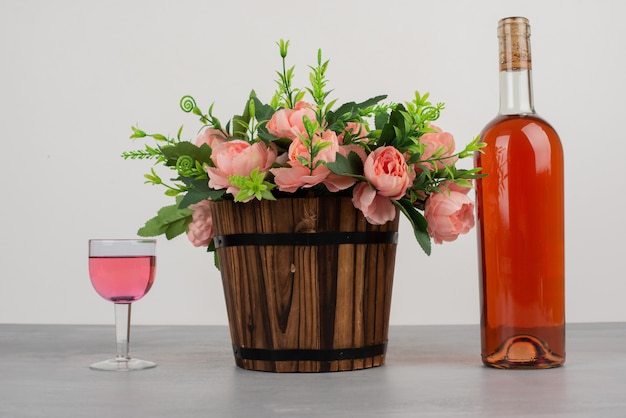 Hermoso ramo de flores y una botella de vino rosado en la mesa gris.