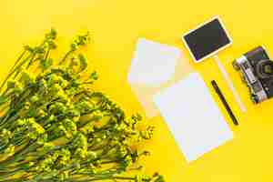 Foto gratuita hermoso ramo de flores; tarjeta; sobre; bolígrafo; cámara y cartel sobre fondo amarillo.