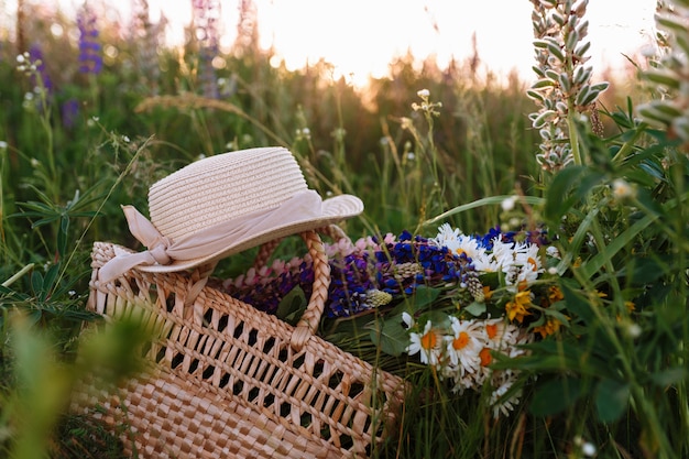 hermoso ramo de lupinos se encuentra en una bolsa junto con un sombrero de paja en la hierba en el campo.