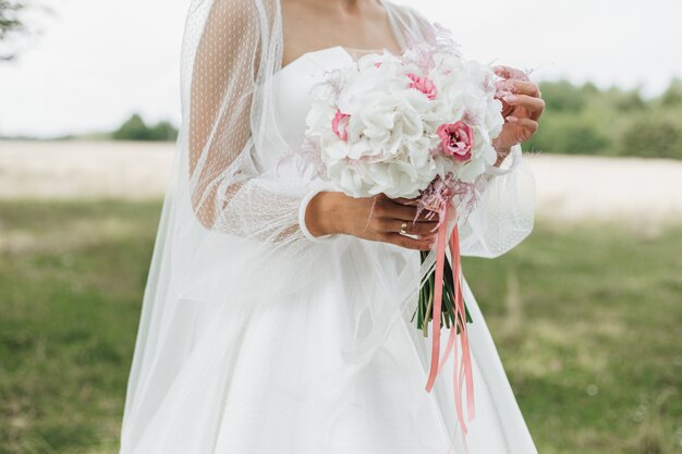 Hermoso ramo de novia hecho de narcisos blancos con middles rosados en las manos de la novia al aire libre