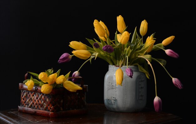 Hermoso ramo de tulipanes amarillos y morados en un jarrón gris sobre la mesa marrón
