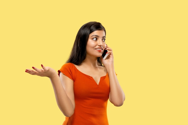 Foto gratuita hermoso retrato femenino de medio cuerpo aislado en espacio amarillo. joven mujer india emocional en vestido hablando por teléfono. espacio negativo