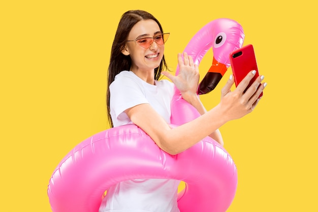 Hermoso retrato femenino de medio cuerpo aislado en la pared amarilla. Mujer sonriente joven en gafas de sol rojas haciendo selfie. Expresión facial, verano, fin de semana, concepto de resort. Colores de moda.