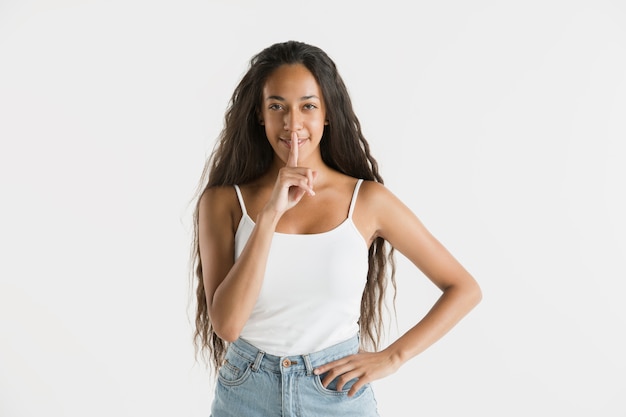 Hermoso retrato femenino de medio cuerpo aislado en la pared blanca. Joven mujer afroamericana emocional con cabello largo. Expresión facial, concepto de emociones humanas. Susurrando un secreto.