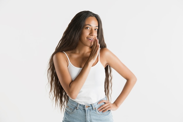 Hermoso retrato femenino de medio cuerpo aislado sobre fondo blanco de estudio. Joven mujer afroamericana emocional con cabello largo. Expresión facial, concepto de emociones humanas. Susurrando un secreto.