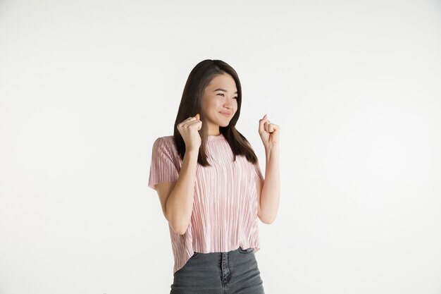 Hermoso retrato femenino de medio cuerpo aislado sobre fondo blanco de estudio. Mujer joven emocional en ropa casual. Las emociones humanas, el concepto de expresión facial. Celebrando como ganador, luce feliz.