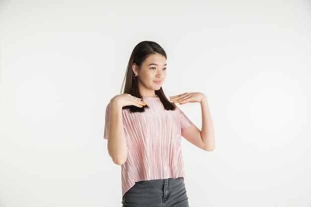 Hermoso retrato femenino de medio cuerpo aislado sobre fondo blanco de estudio. Mujer joven emocional en ropa casual. Las emociones humanas, el concepto de expresión facial. Señalando a sí misma, se ve confiada.