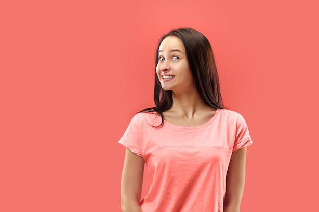 Hermoso retrato frontal de medio cuerpo femenino aislado sobre fondo de estudio coral. Joven mujer sorprendida emocional de pie con la boca abierta.