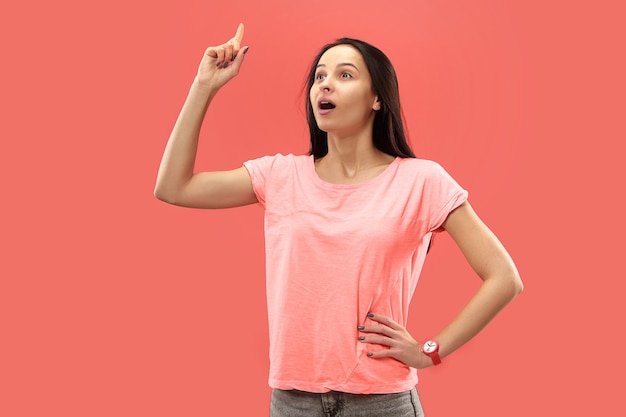 Foto gratuita hermoso retrato frontal de medio cuerpo femenino aislado sobre fondo de estudio coral. joven mujer sorprendida emocional de pie con la boca abierta.