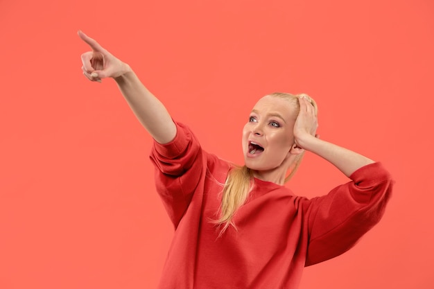 Hermoso retrato frontal de medio cuerpo femenino aislado sobre fondo de estudio coral. Joven mujer sorprendida emocional de pie con la boca abierta.