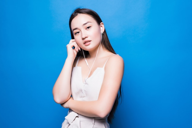 Hermoso retrato joven mujer asiática escuchando música en el teléfono con auricular aislado en la pared azul