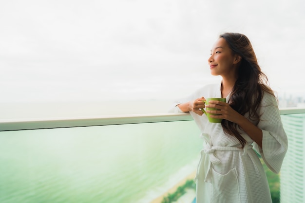 Hermoso retrato de jóvenes mujeres asiáticas sosteniendo la taza de café en el balcón al aire libre con vista al mar