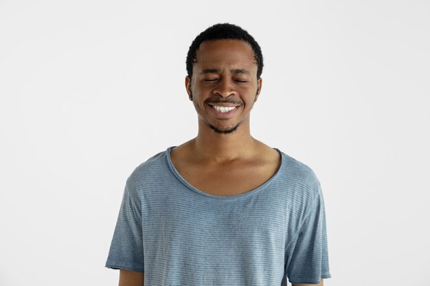 Hermoso retrato masculino de medio cuerpo aislado en la pared blanca. Joven afroamericano emocional en camisa azul. Expresión facial, emociones humanas, concepto publicitario. Riendo, locamente feliz.