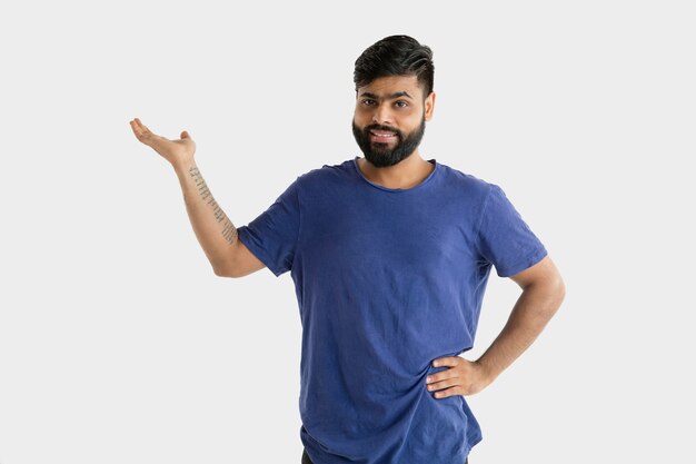 Hermoso retrato masculino de medio cuerpo aislado en la pared blanca. Joven hindú emocional en camisa azul. Expresión facial, emociones humanas, concepto publicitario. Mostrando una barra espaciadora vacía.