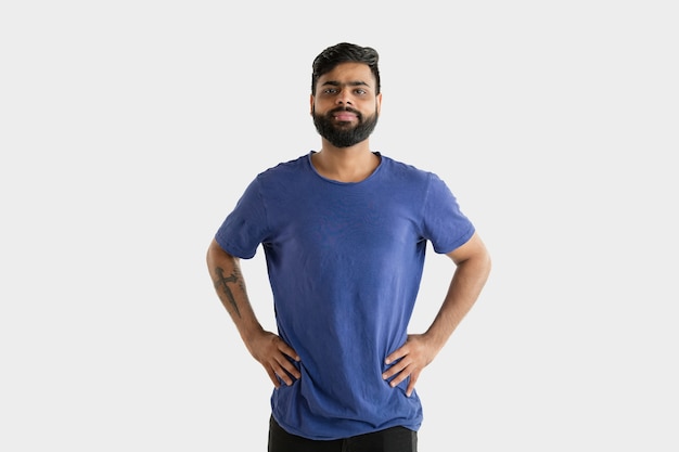 Hermoso retrato de medio cuerpo masculino aislado sobre fondo blanco de estudio. Joven hindú emocional en camisa azul. Expresión facial, emociones humanas, concepto publicitario. De pie y sonriendo.