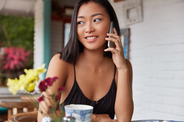 Hermoso retrato de mujer china hablando con el teléfono inteligente en una cafetería