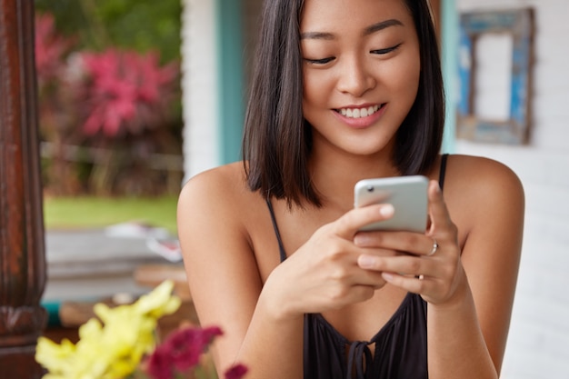 Hermoso retrato de mujer china hablando con el teléfono inteligente en una cafetería