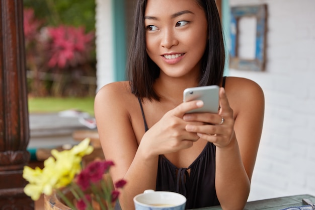 Hermoso retrato de mujer china hablando con el teléfono inteligente en una cafetería