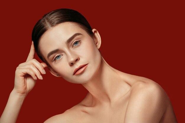 Un hermoso rostro femenino. Piel perfecta y limpia de joven mujer caucásica en estudio rojo.