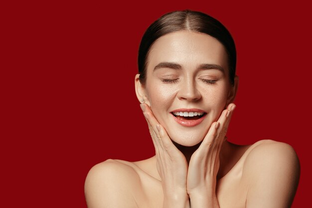 Un hermoso rostro femenino. Piel perfecta y limpia de joven mujer caucásica sobre fondo rojo de estudio.