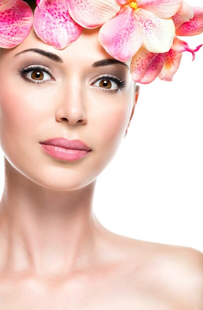 Hermoso rostro de mujer joven y bonita con piel sana y flores rosadas, aisladas en blanco