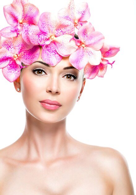 Hermoso rostro de mujer joven y bonita con piel sana y flores rosadas, aisladas en blanco