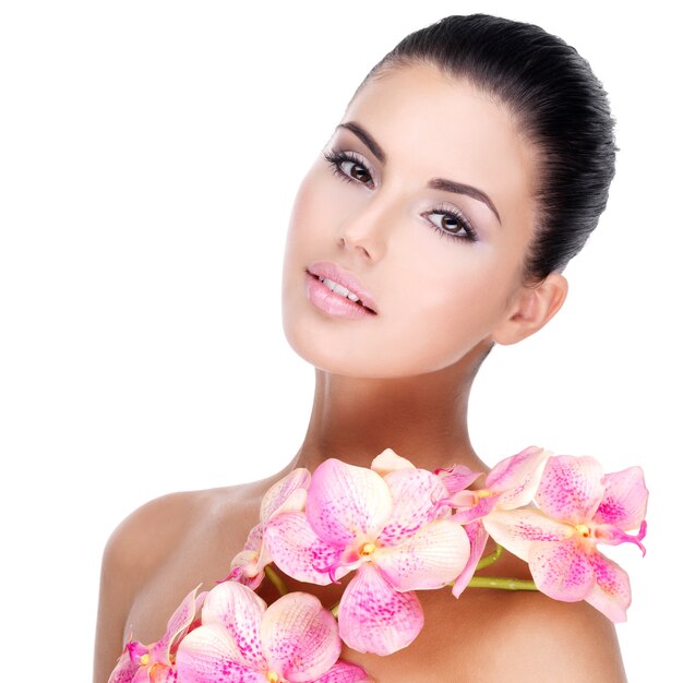 Hermoso rostro de mujer joven y bonita con piel sana y flores rosadas en el cuerpo - aislado en blanco