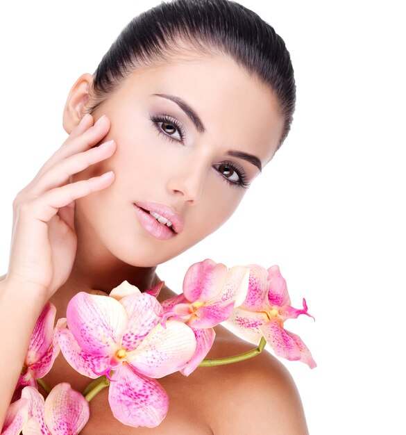 Hermoso rostro de mujer joven y bonita con piel sana y flores rosadas en el cuerpo - aislado en blanco