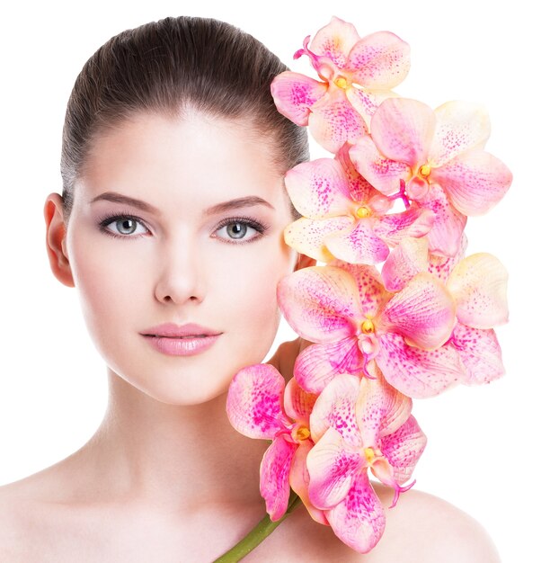 Hermoso rostro de mujer joven morena con piel sana y flores rosadas cerca de la cara - aislado en blanco.