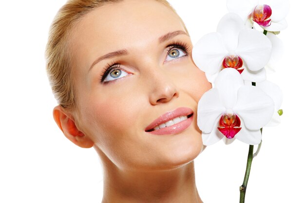 Hermoso rostro de mujer sonriente con flor de orquídea blanca fresca