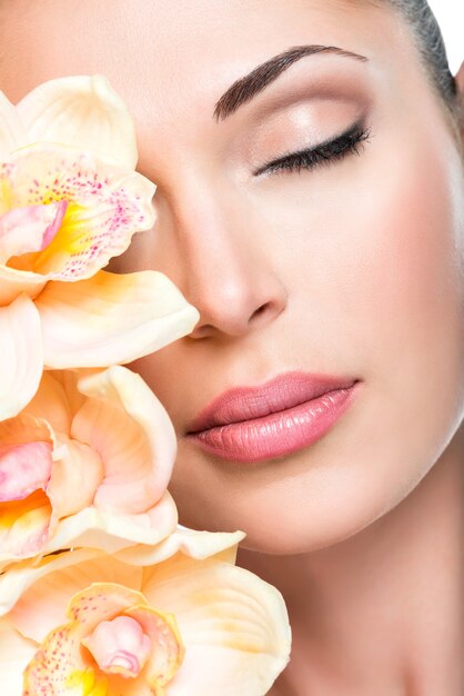 Hermoso rostro relajado de una joven con piel clara y orquídeas rosadas. Concepto de tratamiento de belleza