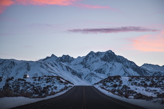 Foto gratuita hermoso tiro ancho de una carretera cerca de montañas llenas de nieve bajo un cielo rosa y morado
