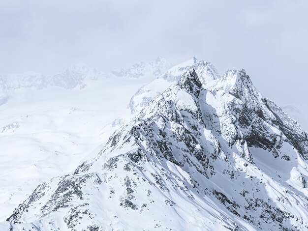 Hermoso tiro ancho de montañas cubiertas de nieve bajo un cielo brumoso