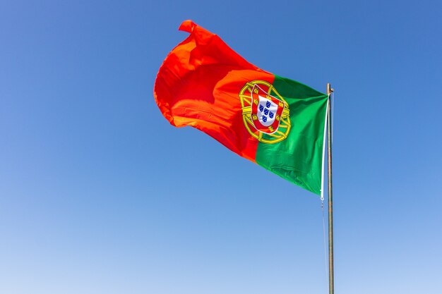 Hermoso tiro de la bandera portuguesa ondeando en el tranquilo cielo brillante