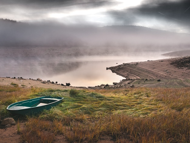 Hermoso tiro de barco verde en una colina cubierta de hierba cerca del mar con niebla