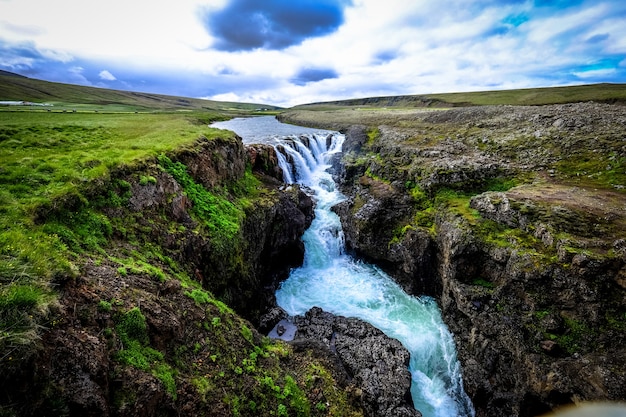 Hermoso tiro de cascada que fluye hacia abajo en medio de colinas rocosas bajo un cielo nublado