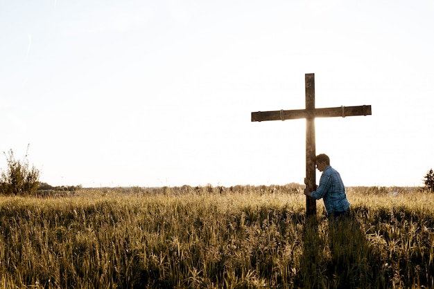 Hermoso tiro de un hombre con la cabeza contra la cruz de madera en un campo de hierba