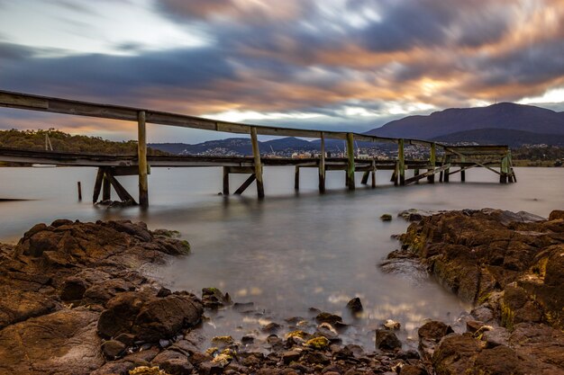 Hermoso tiro de un largo muelle en el agua bajo el colorido cielo nublado