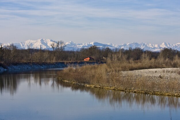 Hermoso tiro de un río en medio de costas y árboles sin hojas con una casa en la distancia