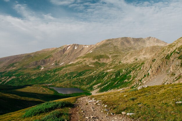 Hermoso tiro de verdes colinas cerca de las montañas con un estanque en la distancia bajo un cielo nublado