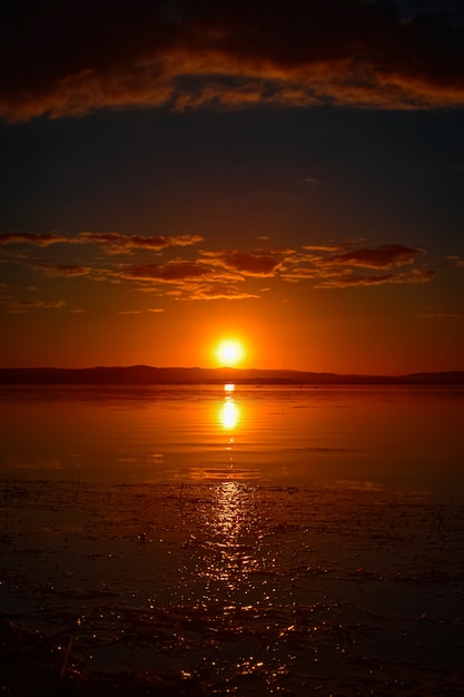 Hermoso tiro vertical de la puesta de sol rojo con nubes en el cielo con reflejo en el agua