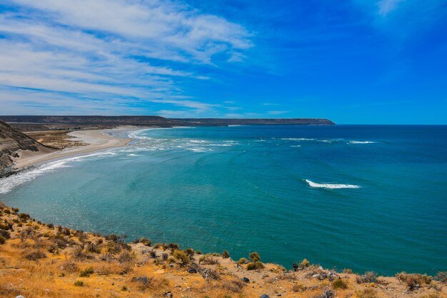 Hermoso y tranquilo océano rodeado por los acantilados bajo el nublado cielo azul