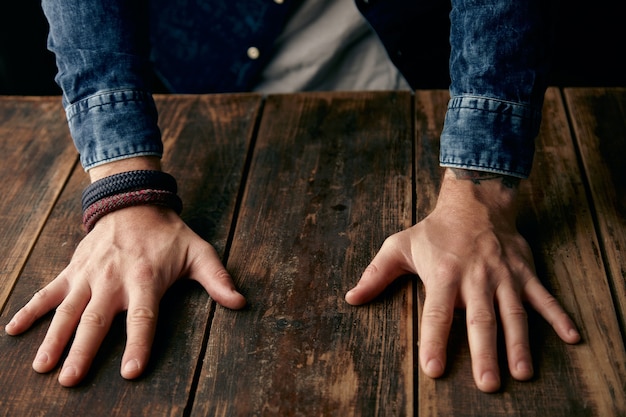 Foto gratuita hermosos hombres con las manos en la mesa, camisa casual de jeans, tatuaje, muñequera, braceletes