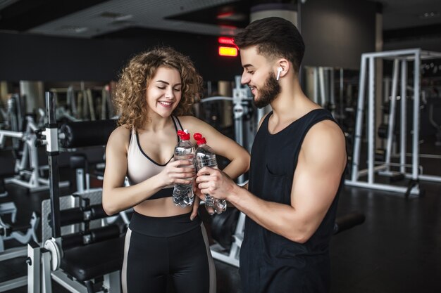 Hermosos jóvenes deportistas sosteniendo botellas de agua, sonriendo durante el descanso